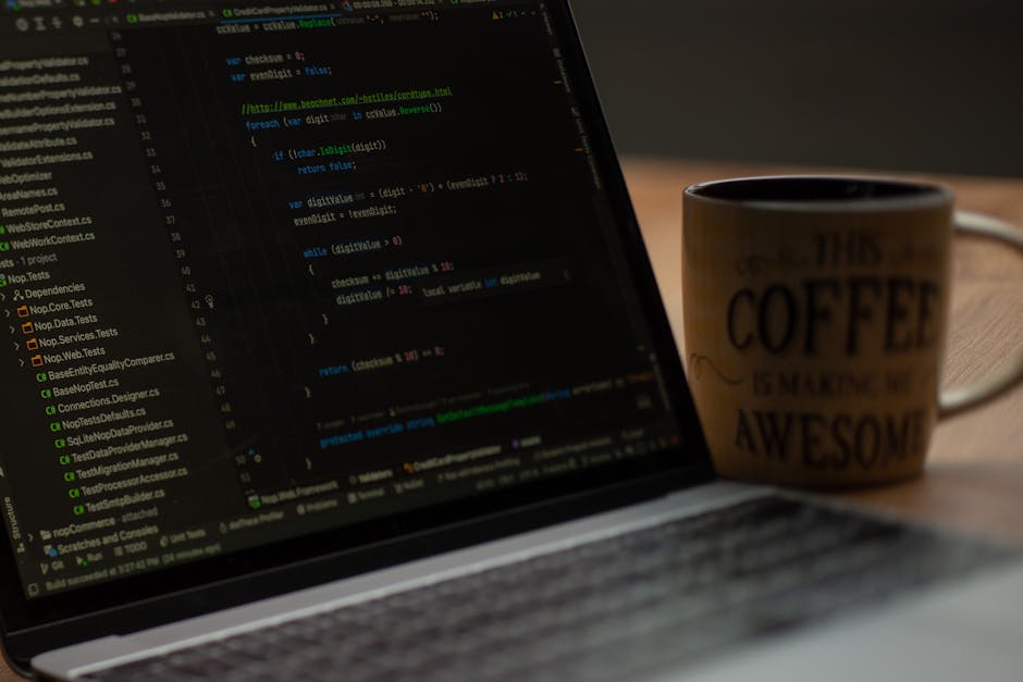 A close-up view of a laptop computer displaying lines of programming code with a dark background and colorful syntax highlighting, placed on a wooden table. To the right of the laptop, there is a cera